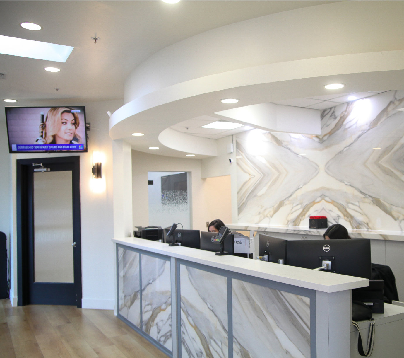 A sleek reception area with a marble desk, computers, and a TV on the wall displaying a news channel.