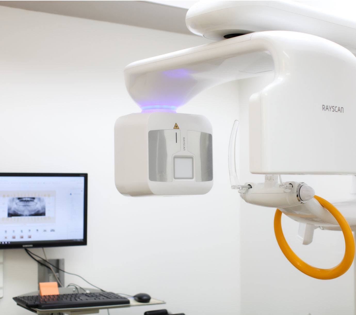 Dental X-ray machine in a clinic with a computer screen displaying an X-ray image in the background.