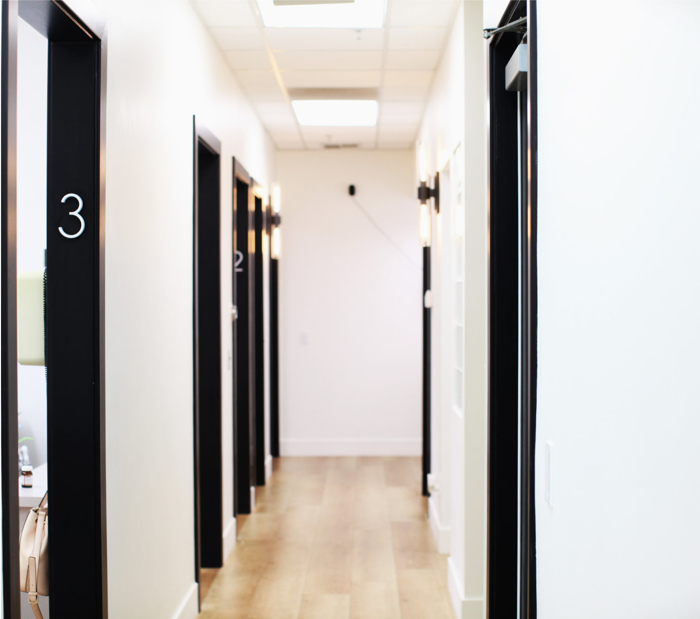 A brightly lit hallway with numbered doors on the left side and a light wood floor.