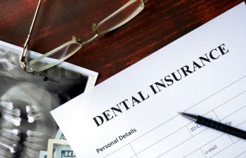 Dental insurance form on a table with a pen, glasses, and an X-ray image.