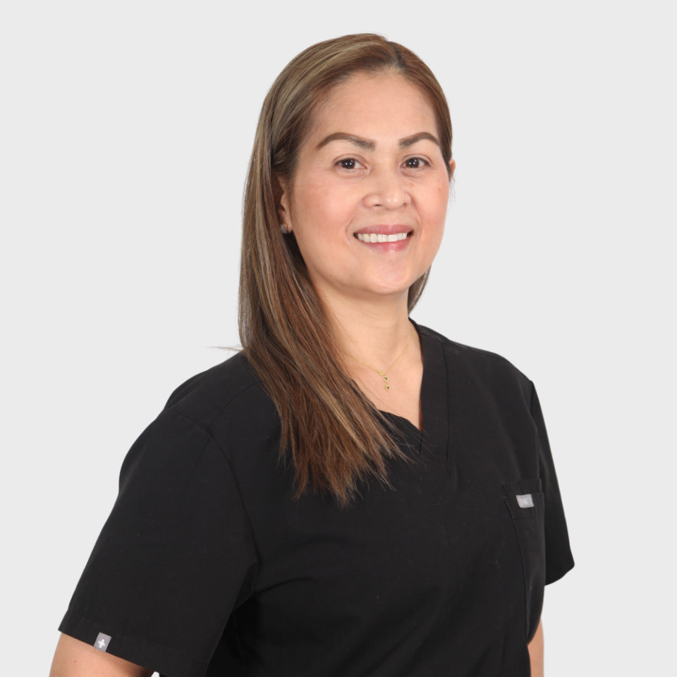 Person with long hair wearing a black top stands against a plain white background, smiling at the camera.