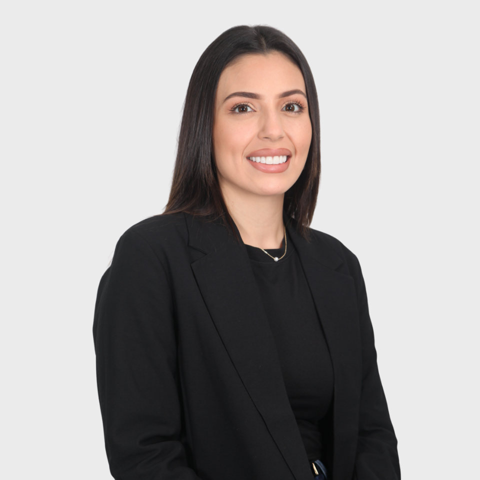 A woman with long hair wearing a black blazer and shirt smiles against a plain white background.