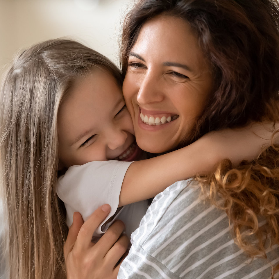 Woman and girl with long hair smiling and embracing each other.