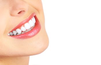 Close-up of a person's smile showing white teeth and glossy pink lips against a white background.