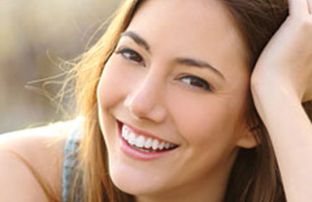 A woman with long hair smiles at the camera, resting her head on one hand.