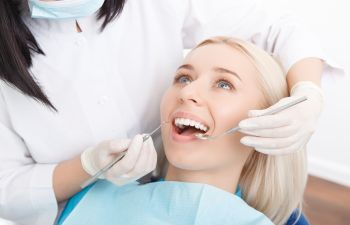 A dentist examines a smiling patient with dental tools.