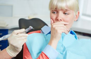 A person sitting in a dental chair looks anxious while a dentist holds a dental tool.