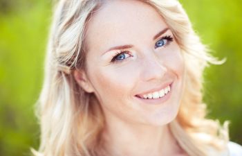 A person with long blonde hair smiling against a blurred green background.