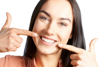 Person smiling and pointing at their teeth with both index fingers, wearing a peach-colored top.