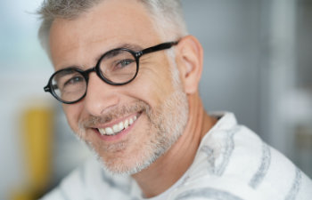 A man with glasses and a graying beard smiles while wearing a striped shirt.